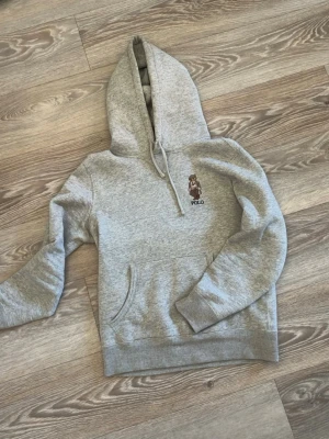 Ralph lauren hoodie - Säljer en grå hoodie från Polo Ralph Lauren med den ikoniska Polo Bear-brodyr på bröstet. Hoodien har huva med dragsko, magficka och ribbade muddar. Perfekt för en avslappnad och stilren look. Andvänd 3 gånger 