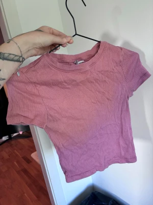 Rosa ribbad croppad t-shirt - Säljer en rosa croppad t-shirt med ribbad struktur och korta ärmar. T-shirten har en rund halsringning och är i ett mjukt material som känns skönt mot huden. Perfekt för en avslappnad och trendig look.