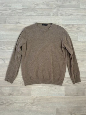 Beige stickad tröja rund hals - En enkel och stilren beige stickad tröja med rund halsringning och långa ärmar. Tröjan har ribbade muddar vid ärmslut och nederkant. Perfekt basplagg för lager på lager och passar till det mesta.