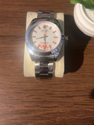 Klocka  - Stilren klocka med silverfärgad länk i metall och vit urtavla. Urtavlan har orange detaljer och tydliga markeringar. Klassisk och tidlös design som passar till många olika stilar. Priset kan diskuteras!