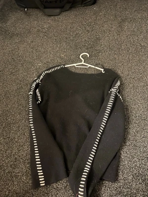 Svart stickad tröja från Y.A.S - Snygg svart stickad tröja från Y.A.S med vita dekorativa sömmar längs ärmar och axlar. Tröjan har en rak passform och långa ärmar, perfekt för dig som gillar en stilren men ändå unik look.