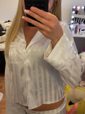 Vit randig satinpyjamas skjorta - Snygg vit pyjamas i glansigt satinmaterial med diskreta vertikala ränder. Detta är annonsen för ENDAST skjortan, hela settet finns att köpa på min profil. I storlek 146/152 från Gina Young