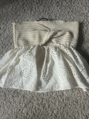 Vit axelbandslös sommarklänning - Söt axelbandslös topp med virkad beige överdel och vit kjol i bomull med broderade blommor. 