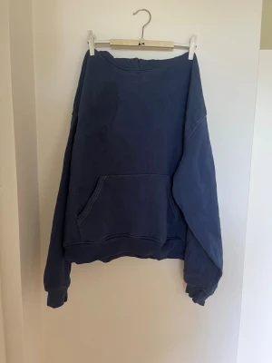 Blå hoodie med ficka - Mysig hoodie i tvättad blå färg med ficka framtill och huva. Tröjan har ribbade muddar vid ärmslut och nederkant. Perfekt för en avslappnad och chill stil. Materialet känns mjukt och behagligt.