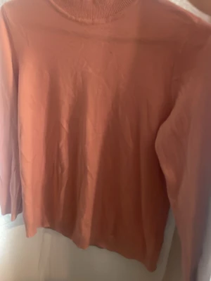 Rosa stickad tröja med polokrage - En enkel och snygg rosa stickad tröja med polokrage. Tröjan har långa ärmar och är tillverkad i ett mjukt material som passar perfekt till kyligare dagar. Stilren modell som är lätt att matcha med olika outfits.