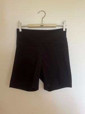 Svarta tajta träningsshorts - Säljer ett par svarta träningsshorts. De är stretchiga och sitter tight, perfekta för träning eller en sportig look. Materialet känns mjukt och följsamt mot kroppen.