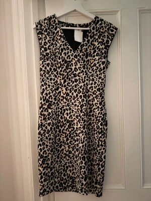 Leopardmönstrad ärmlös klänning - Snygg ärmlös klänning med leopardmönster i svart, beige och bruna toner. Klänningen har v-ringning och en smickrande passform som passar perfekt för dig som vill sticka ut. Tillverkad i ett mjukt och följsamt material.