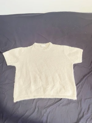 Beige stickad kortärmad topp - En enkel och stilren beige stickad topp med korta ärmar och rund hals. Perfekt för lager på lager eller att bära som den är. Mjuk och bekväm med en avslappnad passform.