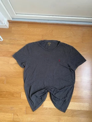 Mörkgrå t-shirt från Polo Ralph Lauren - En enkel och stilren mörkgrå t-shirt från Polo Ralph Lauren med rund halsringning och korta ärmar. Liten röd logga broderad på bröstet. Perfekt basplagg till garderoben. Skickar inom 24h