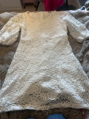 Vit spetsklänning med puffärm - Säljer en vit kortklänning i spets med blommigt mönster och puffiga trekvartsärmar. Klänningen har rund halsringning och är fodrad undertill, vilket ger en romantisk och trendig look. Perfekt för dig som vill sticka ut med en feminin stil.