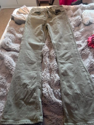 Olivgröna bootcut jeans - Säljer ett par olivgröna jeans med bootcut passform och klassiska fickor fram. Jeansen har en avslappnad look och är tillverkade i ett mjukt bomullsmaterial. Perfekta för dig som gillar en retrostil och vill ha något bekvämt till vardags.