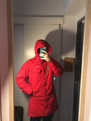 Didriksons Röd parkas - Snygg röd parkas från Didriksons med huva och dragkedja framtill. Jackan har flera praktiska fickor, justerbar midja och quiltat beige innerfoder. Perfekt för kalla dagar och riktigt skön att bära. Klassisk modell som funkar till det mesta.