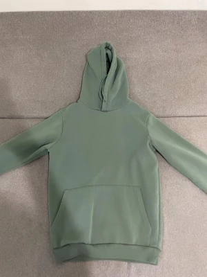 Grön hoodie från SMOG XS - Snygg grön hoodie från SMOG i regular fit. Hoodien har en klassisk känguruficka framtill och en stor huva. Tillverkad i mjukt material som känns skönt mot huden. Perfekt för en avslappnad och stilren look.