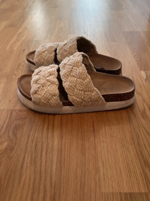 Beige flätade sandaler med platåsula - Säljer ett par snygga sandaler med två breda, flätade band i beige textil. Sandalerna har en bekväm platåsula i vitt och brunt samt öppen tå. Perfekta för en avslappnad och trendig look i sommar.