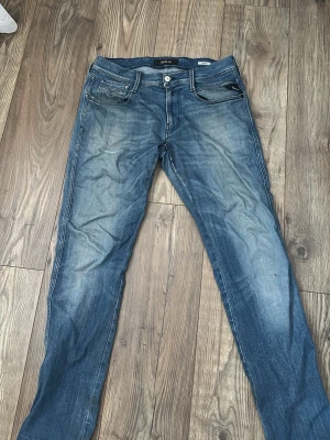 Blå raka jeans från Replay - Snygga blå jeans från Replay med raka ben och klassisk femficksmodell. Jeansen har en lätt tvättad look med slitningar och detaljerade sömmar. Tillverkade i bomull för en bekväm känsla och passar perfekt till en avslappnad stil.