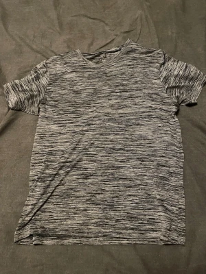 Grå t-shirt  - Snygg gråmelerad t-shirt med ett diskret mönster i olika grå nyanser och är tillverkad i ett mjukt och stretchigt material som känns skönt mot huden. Perfekt för en avslappnad och stilren look.