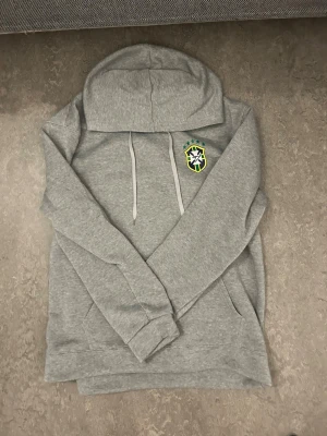 Grå Brazil Hoddie - En Grå brasiliansk hoodie som är helt ny. Råkat köpa fel storlek och tvingas därefter att sälja den för billigare. Kvaliteten på hoodien är extremt bra då den är 100% äkta. Priset kan även Diskuteras. Storleken är S men XS och M kan använda hoodien också👌