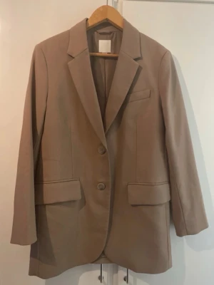 Beige H&M Kavajset - Beige oversized kavajset från H&M som använts ett par gånger men är i bra skick. Finns en liten trasig söm i fodret, men den kan sys ihop. Dessutom har byxorna sytts lite kortare, men det går att sprätta upp.  Säljs tillsammans.