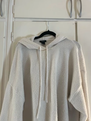 Stickad vit hoodie från Lindex - Mysig beige hoodie från Lindex i storlek S. Tillverkad i ett mjukt, strukturerat tyg med huva och dragsko. Perfekt för en avslappnad och chill stil. Långa ärmar och rymlig passform gör den extra bekväm.