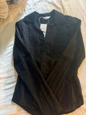 Svart skjorta från Cubus i viskos - Stilren svart skjorta från Cubus i tunn, lätt och skrynklig viskosblandning. Skjortan har klassisk krage, knappar framtill och lång ärm. Perfekt för dig som gillar en enkel men trendig look.