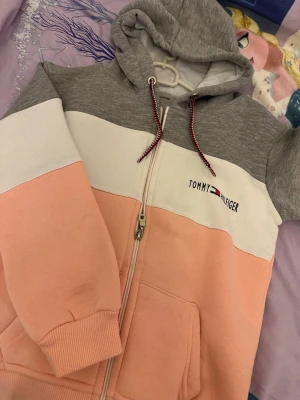  mjukisset i pastell - Säljer ett snyggt mjukisset med hoodie och byxor. Setet har färgblock i grått, vitt och ljusrosa, dragkedja framtill och fickor. Logga broderad på både tröja och byxa. Tillverkat i mjuk bomullsblandning för maximal komfort.