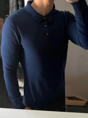 Mörkblå långärmad polotröja - Snygg mörkblå långärmad polotröja från John Henric. Tröjan har klassisk krage, tre knappar framtill och är tillverkad i mjukt material som ger en stilren look. Perfekt till jeans eller chinos för en clean outfit. Storlek m men är  liten i storleken så sitter som s. 100% merinoull 
