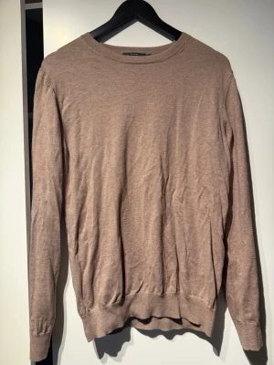 Beige tröja från Dressmann - Snygg beige tröja från Dressmann i mjuk Supima-bomull. Tröjan har rund halsringning, långa ärmar och ribbade muddar vid ärmslut och nederkant. Enkel och stilren design som passar till många olika outfits.