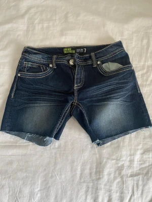 Mörkblå denimshorts med rå kant - Säljer ett par mörkblå jeansshorts från Wallbase med rå, avklippt kant och kontrastsömmar. Shortsen har fem fickor och superlåg midja. Perfekta för sommardagar och har en klassisk denimlook.