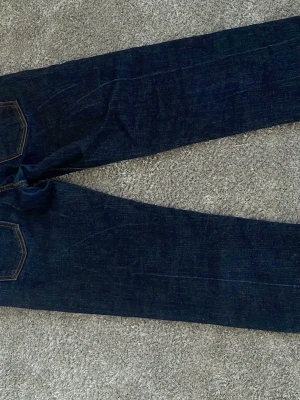 Nudie jeans - Säljer ett par mörkblå jeans med raka ben och klassiska kontrastsömmar. Jeansen har fem fickor och knappgylf. Perfekta till en avslappnad stil och funkar året runt. Materialet är kraftig denim i bomull. 30/30