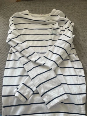 Randig långärmad topp Les Deux - Säljer en vit långärmad topp från Les Deux med marinblå horisontella ränder. Klassisk och stilren design med rund halsringning. Perfekt för dig som gillar en enkel men snygg look. Tillverkad i mjuk bomull för skön känsla.