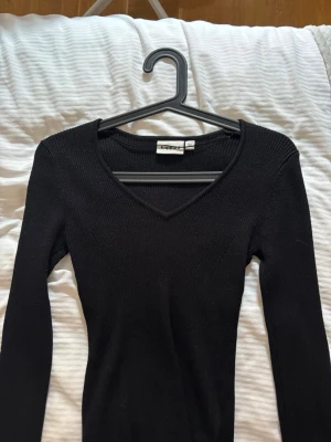 Svart glittrig tröja från Kappahl - Snygg svart glittrig tröja från Kappahl med V-ringning och lång ärm. Tröjan har en smal passform och ribbstickad struktur som ger en stilren look. Perfekt att matcha med jeans eller kjol för en enkel men trendig outfit.
