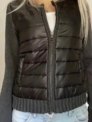 Svart Cardigan jacka  - Snygg svart pufferjacka med quiltad front och rygg i glansigt material samt stickade grå ärmar och muddar. Jackan har dragkedja framtill och två fickor. Liknar Monclers cardigan ⭐️