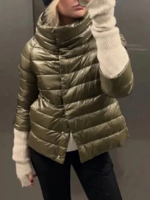 Olivgrön Herno jacka - Snygg olivgrön dunjacka med glansig finish och breda, horisontella kanaler. Jackan har en hög, vadderad krage och dold dragkedja framtill. Nypris: 5500kr