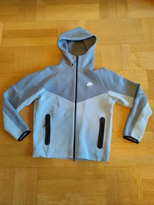 Nike Tech Gen 4 Baby Blue Set - .Säljer ett komplett Nike Tech Gen 4 set i baby blue med en lite mörkare blå ton upptill. Både hoodie och byxor är i storlek M.                                                                   Setet är i fint skick och väldigt bekvämt, men säljs eftersom det tyvärr inte passar mig längre. Pris: 1000 kr (kan diskuteras vid snabb affär). Hör av dig vid frågor eller om du vill ha fler bilder! Den har litte smuts på högra benet men det syns knappt 