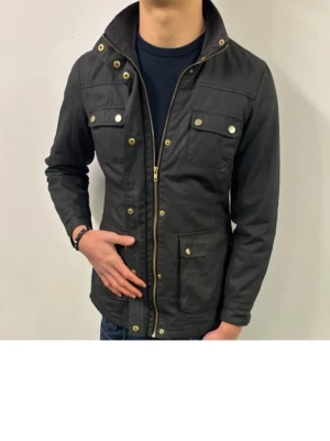 Tvärfet field jacket!! - Stilren svart jacka med quiltat innerfoder och flera praktiska fickor med tryckknappar. Jackan har dragkedja framtill och detaljer i guld. Perfekt för dig som vill ha en snygg och funktionell jacka till vardags eller mer festliga tillfällen. Vid minsta fråga eller fundering är de bara att skriva, priset går att diskuteras. 