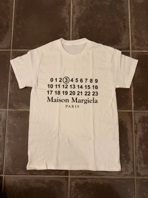 Maison margiela t shirt - Riktigt fet och eftertraktad t-shirt med Maison marinena loggan i storlek S. Väldigt bra skick!  Obs: Jag är lite osäker på äktheten då lappen i nacken saknas, därför säljs den billigare (499 kr, nypris ca 3000 kr).  längd cirka 65cm, bredd cirka 44cm. Tveka inte att höra av dig vid frågor eller funderingar!