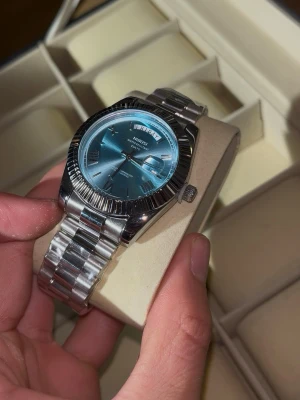 Ekstrand DayDate Ljusblå/Silver - Stilren klocka från med president armband i silver med en ljusblå urtavla, skriv vid funderingar 