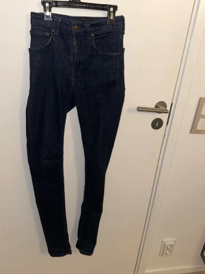 Mörkblå skinny jeans från Nudie Jeans - Snygga mörkblå skinny jeans från Nudie. Jeansen har en smal passform och är gjorda i stretchigt denimtyg. Nudie-logga på bakfickan och läderpatch i midjan. Perfekta till en avslappnad streetstyle-look.