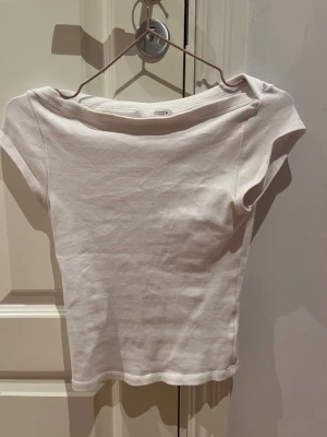 Vit ribbad topp med bred hals - Säljer en enkel och stilren vit ribbad topp med bred, nedvikt halsringning och korta ärmar. Toppen är figurnära och gjord i ett mjukt, stretchigt material som passar perfekt till jeans eller kjol. Märket är Zara .