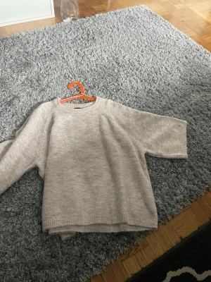 Beige stickad tröja från 157 - Mysig beige stickad tröja från 157 med rund halsringning och avslappnad passform. Tröjan har ribbade muddar vid hals, ärmslut och nederkant. Perfekt för lager på lager och enkel att matcha med jeans eller kjol.