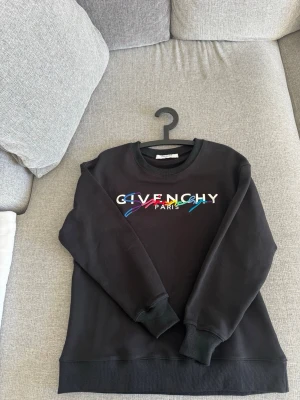 Svart Givenchy sweatshirt med färgglad logga - Snygg svart sweatshirt från Givenchy med färgglad broderad logga på bröstet och texten 'Paris' under. Tröjan har rund halsringning, ribbade muddar vid ärmslut och nederkant. Perfekt för dig som vill ha en trendig och exklusiv look.