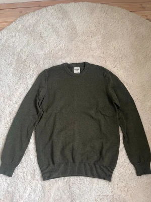 Olivgrön stickad tröja från Dobber - Snygg olivgrön stickad tröja från Dobber med rund halsringning och ribbade muddar vid ärmslut och nederkant. Perfekt för lager på lager och enkel att matcha med jeans eller linnebyxor. Klassisk och stilren design.