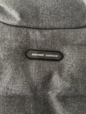 Mörkgrå cardiganjacka Jack & Jones - Oanvänd Mörkgrå cardiganjacka från Jack & Jones Premium med quiltad kropp och stickade ärmar. Jackan har ståkrage, dragkedja framtill och två fickor med tryckknappar. Materialmixen ger en modern och stilren look.