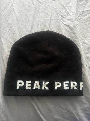 Svart mössa från Peak Performance - Säljer en svart mössa från Peak Performance med vit text runt om nederkanten. Klassisk och enkel design i mjukt stickat material som passar perfekt till kalla dagar. Snygg och stilren accessoar för dig som gillar sportigt mode. Endast legat i en låda, aldrig använt. Nypris ca 450-500kr. Kom gärna med prisförslag 