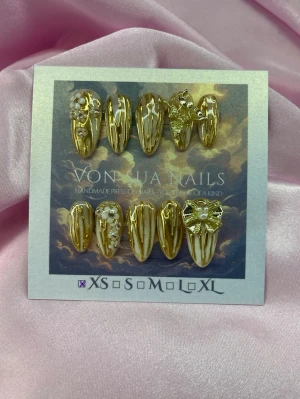 Aurelia (XS);Medium Almond - Handgjorda Lyxiga press-on naglar i guld med vit/nude ombre detaljer, pärlor och 3D-dekorationer som blommor, fjäril och rosett. Naglarna har en medium lång almond-form och skimrande finish. Perfekt för dig som vill sticka ut med glamorösa och unika naglar.XS: 14 mm, 11 mm, 11,5 mm, 10 mm, 8 mm 