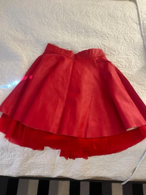 Röd volangkjol med hög midja - Snygg röd kjol med volang och hög midja. Kjolen har en kort längd och flera lager tyg som ger extra volym och en cool look. Perfekt för dig som vill sticka ut med en färgstark och trendig stil.