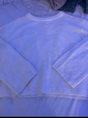 Vit stickad tröja med rund hals - Mysig vit stickad tröja med rund hals och långa ärmar. Tröjan har en enkel och klassisk design med ribbstickade muddar vid hals, ärmslut och nederkant. Perfekt för lager på lager och passar till det mesta.