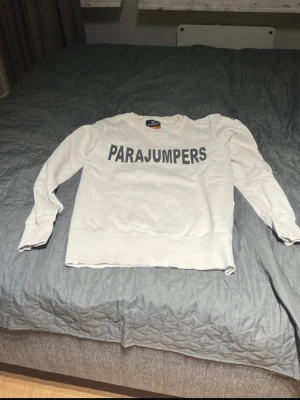 Vit sweatshirt från Parajumpers - Snygg vit sweatshirt från Parajumpers med stor logga i grått över bröstet. Tröjan har rund halsringning, långa ärmar och ribbade muddar vid ärmslut och nederkant. Perfekt för en avslappnad och trendig look.