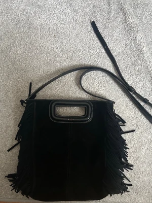 Svart stor majeväska i mocka - Snygg svart axelväska från Maje i mocka med fransar längs sidorna. Väskan har både avtagbar axelrem och ett rektangulärt handtag i svart läder. Köpt för 2800kr men är dyrare att köpa ny nu! Hör gärna av er vid frågor t.ex äkthetsbevis eller fler bilder. Gör gärna prisförslag!