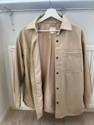 Beige overshirt från HM - Stilren beige overshirt från HM i storlek S. Skjortjackan har tryckknappar, en bröstficka och klassisk krage. Materialet ser ut att vara mjukt och lätt, perfekt för lager på lager. Enkel att matcha med olika outfits. Pris diskuteras gärna!